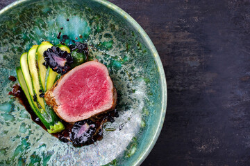 Modern style traditional fried dry aged angus beef filet medaillons natural with baby zucchini, lettuce and forest berries served as top view in a design bowl with copy space left
