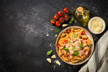 Italian pasta alla arrabiata with basil and parmesan cheese on dark table. Fusilli pasta with tomato sauce arrabbiata. Top view.