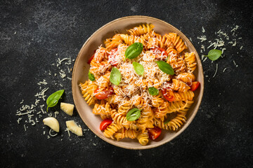 Traditional Italian pasta with tomato sauce, basil and parmesan on black table. Fusilli pasta with tomato sauce arrabbiata. Top view.