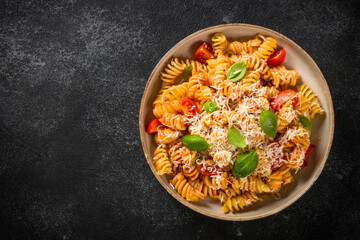 Italian pasta alla arrabiata with basil and parmesan cheese on dark table. Fusilli pasta with tomato sauce arrabbiata. Top view.