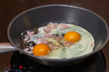 Two fried eggs in a pan on the stove. Two whole yolks are visible and there is white egg around. There is salami in the egg.