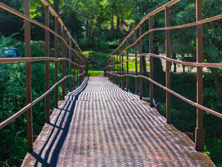 Close up of a narrow metal foot bridge, green nature background