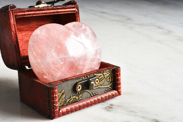 A close up image of a heart shaped rose quartz crystal in a small wooden box.  
