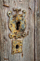 A keyhole made of rust-covered iron in the Middle Ages style is located on an old wooden door. Spain.
