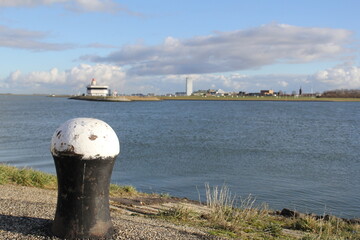 The estuary of the canal Ghent Terneuzen in the westerschelde sea and the skyline of Terneuzen in the background and a bollard at the quay in front and a blue sky
