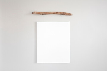 Blank vertical poster mockup hanging by a simple driftwood frame on a neutral brown coloured wall. 