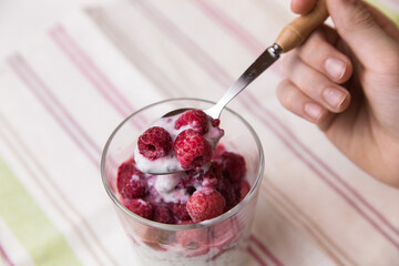 The hands of the child hold a glass with a dessert of yogurt, chia seeds, frozen raspberries ,close-up