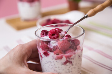 The hands of the child hold a glass with a dessert of yogurt, chia seeds, frozen raspberries
