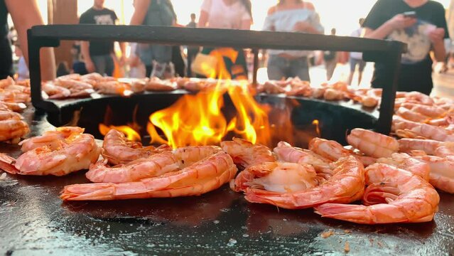 Close up footage of process of grilling fresh king prawns on brazier with hot flame at summer days, a hand in rubber gloves lays out king prawns on a hot iron surface, fresh seafood,