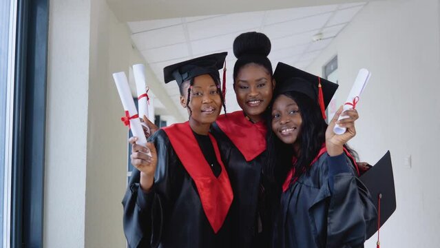 African american university woman graduates stand in front of the camera in master's hats and black robes. Prosess of university studies. Master of Science