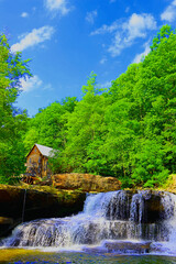 Fototapeta na wymiar Water Grist Mill Babcock State Park West Virginia. Water wheel. Stream or creek with waterfall . Summer. Green trees. Blue sky. White clouds. Country. USA. Peaceful and relaxing. Grist Mill. Wild