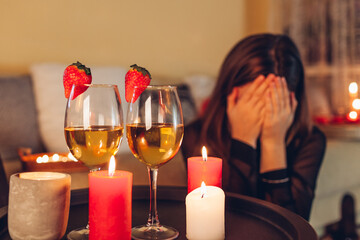 Sad woman crying at home by romantic table setting with wine glasses. Left alone and brokenhearted on Valentine's Day