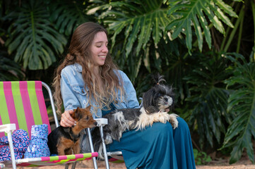 One woman sitting on a beach chair with a lhasa apso on her lap and one mixed breed dog on another...