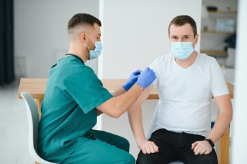 Obraz premium medicine, vaccination and healthcare concept - doctor wearing face protective medical mask for protection from virus disease with syringe doing injection of vaccine to male patient