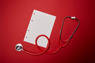 Medical clinical red stethoscope doctor health care tool equipment with receipt blank copy space sheet isolated on the bright solid fond plain red background