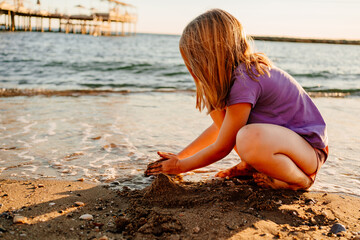 a cute little girl sits on the seashore, playing in the sand and with pebbles. 