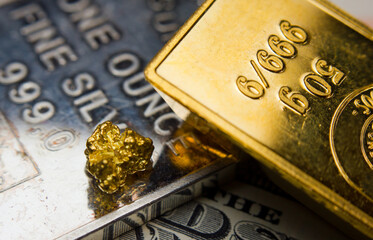 Close-up of a gold ingot on top of a troy ounce silver and coin
