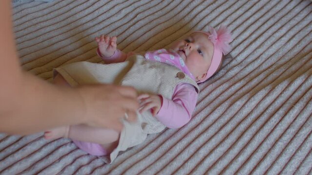 Portrait of six-month-old baby actively moves her arms and legs. Mom's hand straightens the clothes on the little girl before the home child photo shooting. 