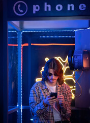 Night Man using smartphone in old phone box at night with neon light 