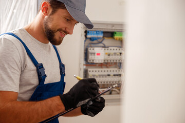 Busy electrical technician writing on a clipboard the data collected on a residential electric panel