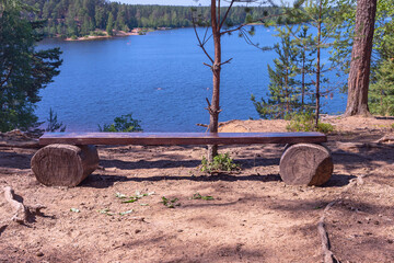a simple wooden bench on a steep sandy shore near a forest lake. Karelia, Russia