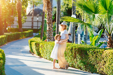 mom and daughter in hats walk along the path in the tropical park of the hotel