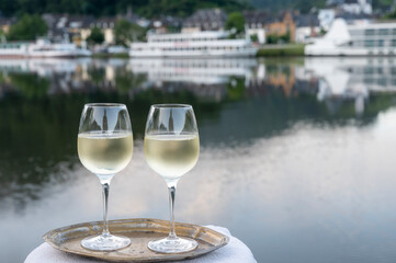 Tasting of white quality riesling wine served on outdoor terrace in Mosel wine region with Mosel river and old German town on background, Germany