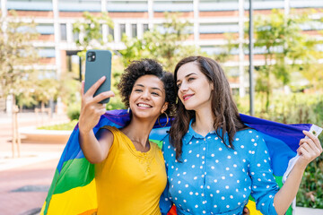 Smiling multiethnic lesbian couple with rainbow flag taking selfie
