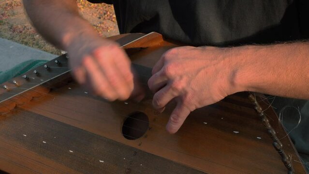 Musician hands beat the strings rhythmically. A man holds gusli on his lap and plays. Soft daylight. Close-up.