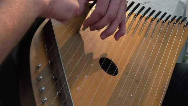 Musician hands beat the strings rhythmically. A man holds gusli on his lap and plays. Soft daylight. Close-up.