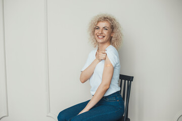 Woman getting vaccinated against covid-19, showing arm with adhesive bandage while sitting on...