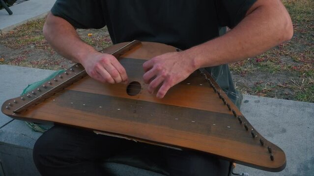 Musician hands beat the strings rhythmically. A man holds gusli on his lap and plays. Soft daylight. Close-up.