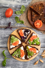 Grain rye bread sandwiches with cream cheese, tomatoes and microgreen on gray background. top view