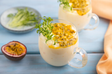 Mango yogurt with passionfruit and cilantro microgreen in glass on blue. Side view, selective focus.