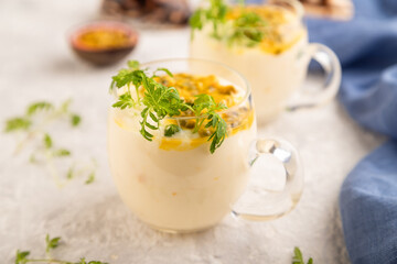 Yogurt with passionfruit and marigold microgreen in glass on gray. Side view, selective focus.