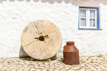 a millstone to produce olive oil and a metal oil barrel in front of a white house for decoration
