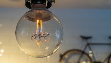 Efficient incandescent light bulb waste electricity against a tiled wall with a small bike and a...