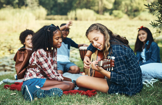 What's summer camp without a singalong. Shot of a group of teenagers playing musical instruments in nature at summer camp.