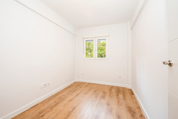 Empty room with chestnut wood flooring with a window looking out onto the garden area