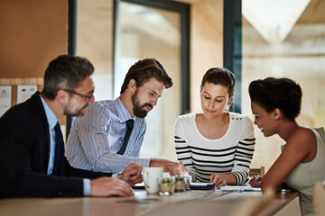 Using technology to explain his ideas. Shot of a group of colleagues using a digital tablet together while working around a table in an office.