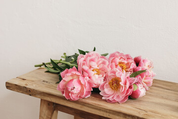 Blooming pink peonies flowers, bouquet lying on old wooden table, bench. White wall. Selective focus, blurred background. Wedding or birthday celebration, gift concept. Floral still life. © tabitazn