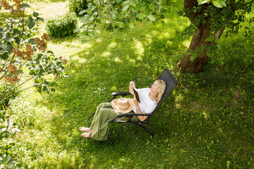 Woman reading a book in garden recliner chair. Summer vacation in the yard. Mature Scandinavian...
