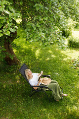 Fototapeta premium Woman reading a book in garden recliner chair. Summer vacation in the yard. Mature Scandinavian female life in retirement. Good living. View from the top. Beautiful middle aged woman resting