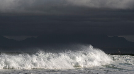 Seascape. Powerful ocean wave on the surface of the ocean. Wave breaks on a shallow bank. Stormy weather, stormy clouds sky background.