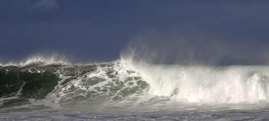 Seascape. Powerful ocean wave on the surface of the ocean. Wave breaks on a shallow bank. Stormy weather, stormy clouds sky background.