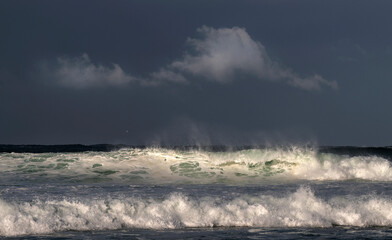 Seascape. Powerful ocean wave on the surface of the ocean. Wave breaks on a shallow bank. Stormy weather, stormy clouds sky background.