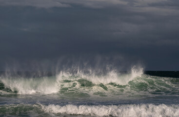 Seascape. Powerful ocean wave on the surface of the ocean. Wave breaks on a shallow bank. Stormy weather, stormy clouds sky background.