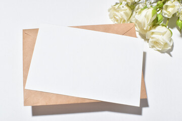 A kraft envelope and a blank sheet of paper with white bush roses on a white background. Banner for Valentine's Day. Invitation to a wedding, anniversary, birthday.