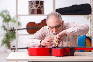 Old male repairman repairing musical instruments at workplace