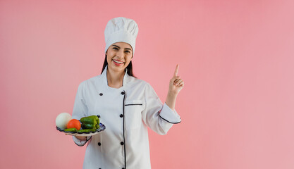 young latin woman wearing chef hat with ingredients to cook mexican food on pink color background